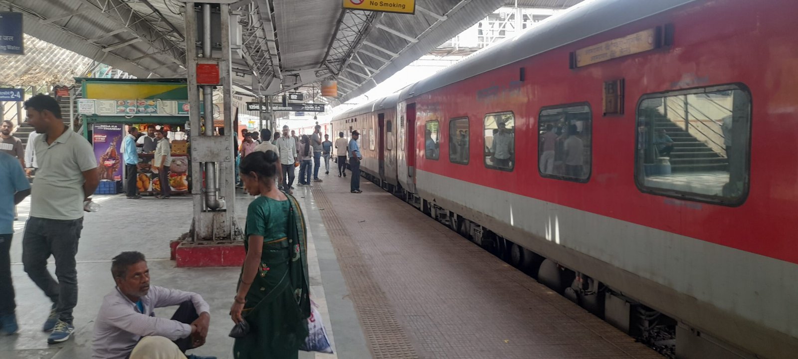 Passengers at a railway station in Agra, Uttar Pradesh, with railway tracks, platforms, and station infrastructure visible.